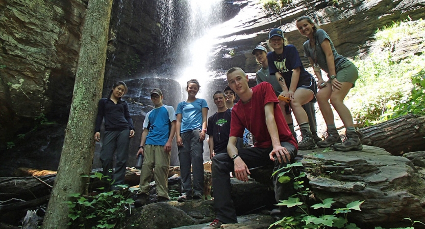 A group of students pose for a photo in front of a waterfall. 